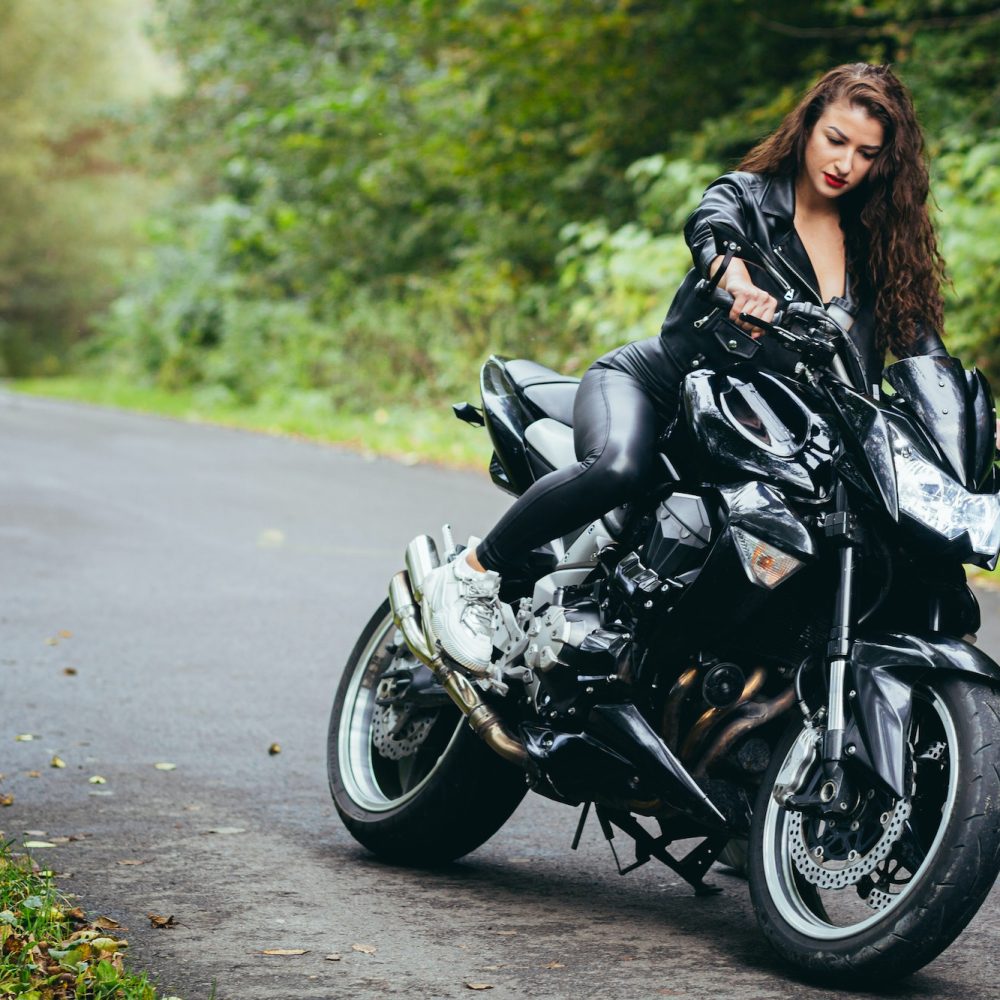 Portrait of a beautiful young woman sitting on a motorcycle, riding a motorcycle in black leather